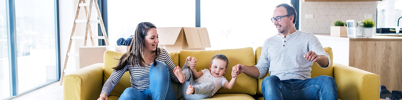 Eine Familie freut sich auf einem gelben Sofa über ihre neue Eigentumswohnung