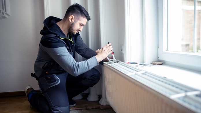 Handwerker, der eine Heizung in einem Wohnraum einbaut und mit einer Zange fixiert.