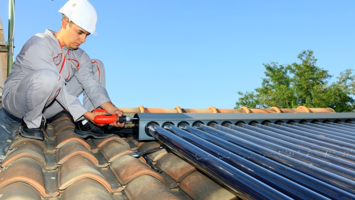 Ein Handwerker in Montur bringt auf einem Dach eine Solarthermieanlage an