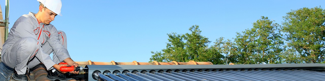 Ein Handwerker in Montur bringt auf einem Dach eine Solarthermieanlage an