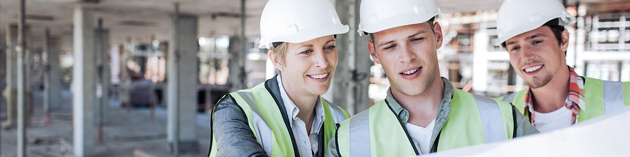 Drei Personen auf einer Baustelle, die gemeinsam auf ein großen Plan schauen.