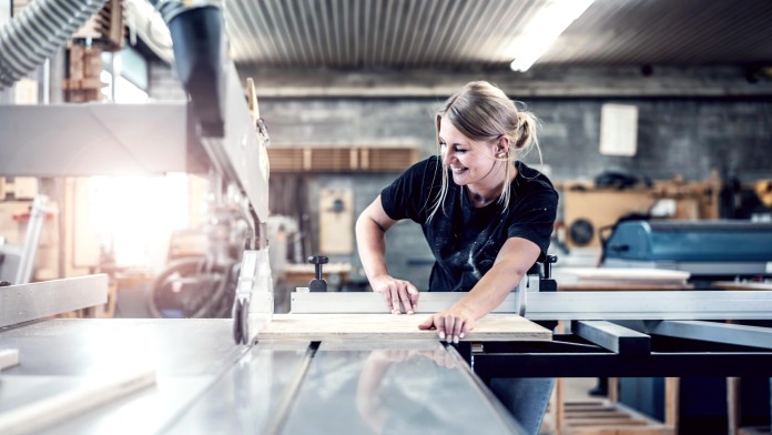 A blonde woman works in a carpenter's workshop
