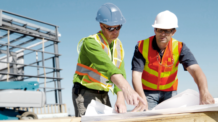 Zwei Architekten auf einer Baustelle blicken auf eine Bauzeichnung