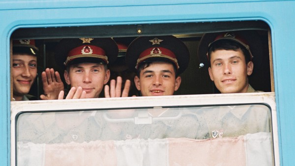 Soviet soldiers smiling and waving from the window of a train. 